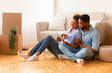 Couple assis sur le sol parmi des cartons de déménagement déballés (English would be: Couple sitting on floor among unpacked moving boxes)